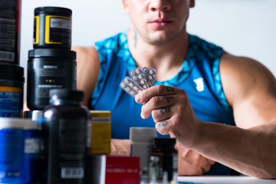 Male bodybuilder holding a packet of legal Deca-Durabolin alternative supplements.