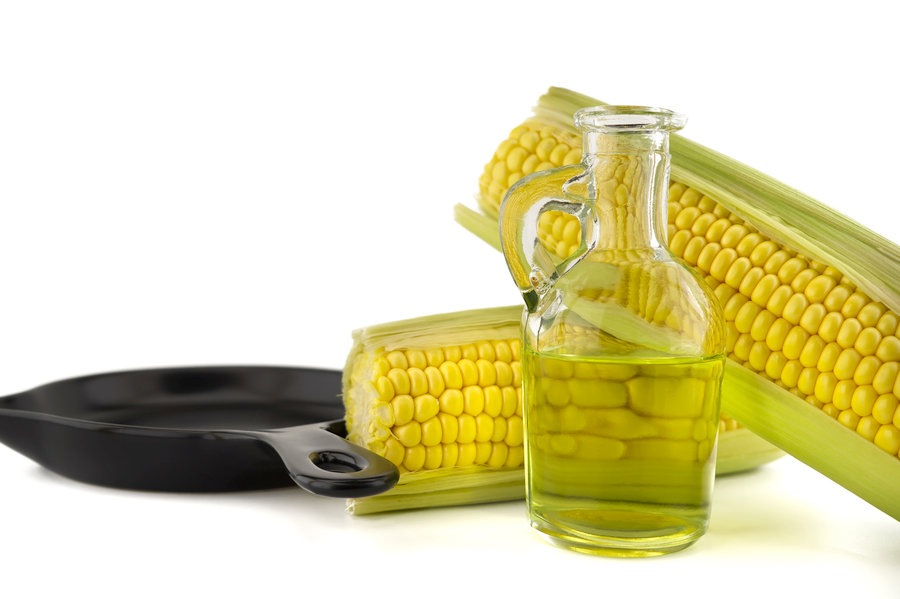 A bottle of corn oil, next to corn cobs and a frying pan